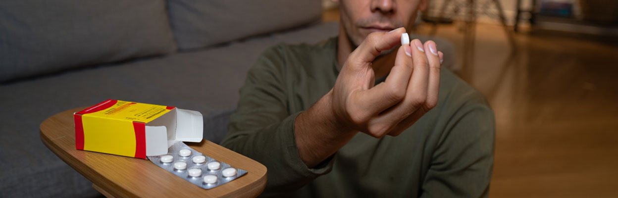 Мужчина держит таблетку в руках, рядом лежит упаковка лекарств